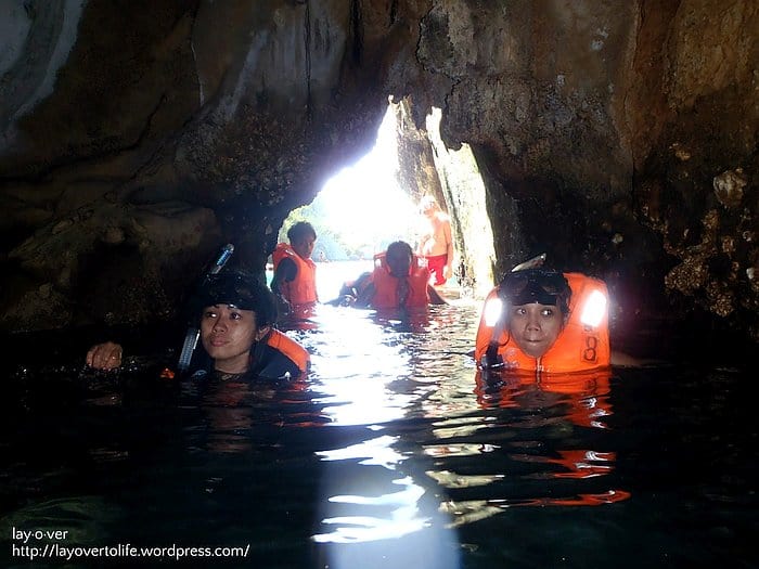 People wearing life jackets and snorkeling gear explore a cave partially submerged in water, all part of an unforgettable boat tour in El Nido.