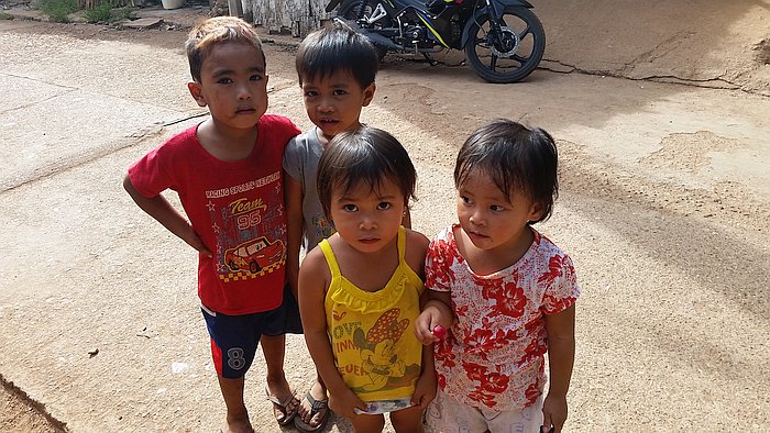 Four children stand together on a concrete path, dressed in casual summer clothes and gazing at the camera. A parked motorcycle rests in the background, capturing a slice of daily life in rural Coron.