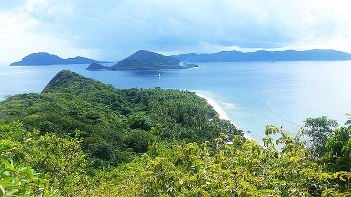 Experience a scenic view of lush green islands with sandy beaches, surrounded by the calm blue ocean under a partly cloudy sky, perfect for a relaxing boat trip.