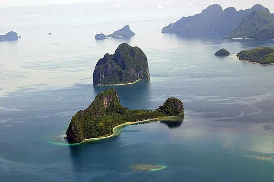 Aerial view of small, lush green islands with rocky cliffs surrounded by calm blue water, perfect for an El Nido boat tour.