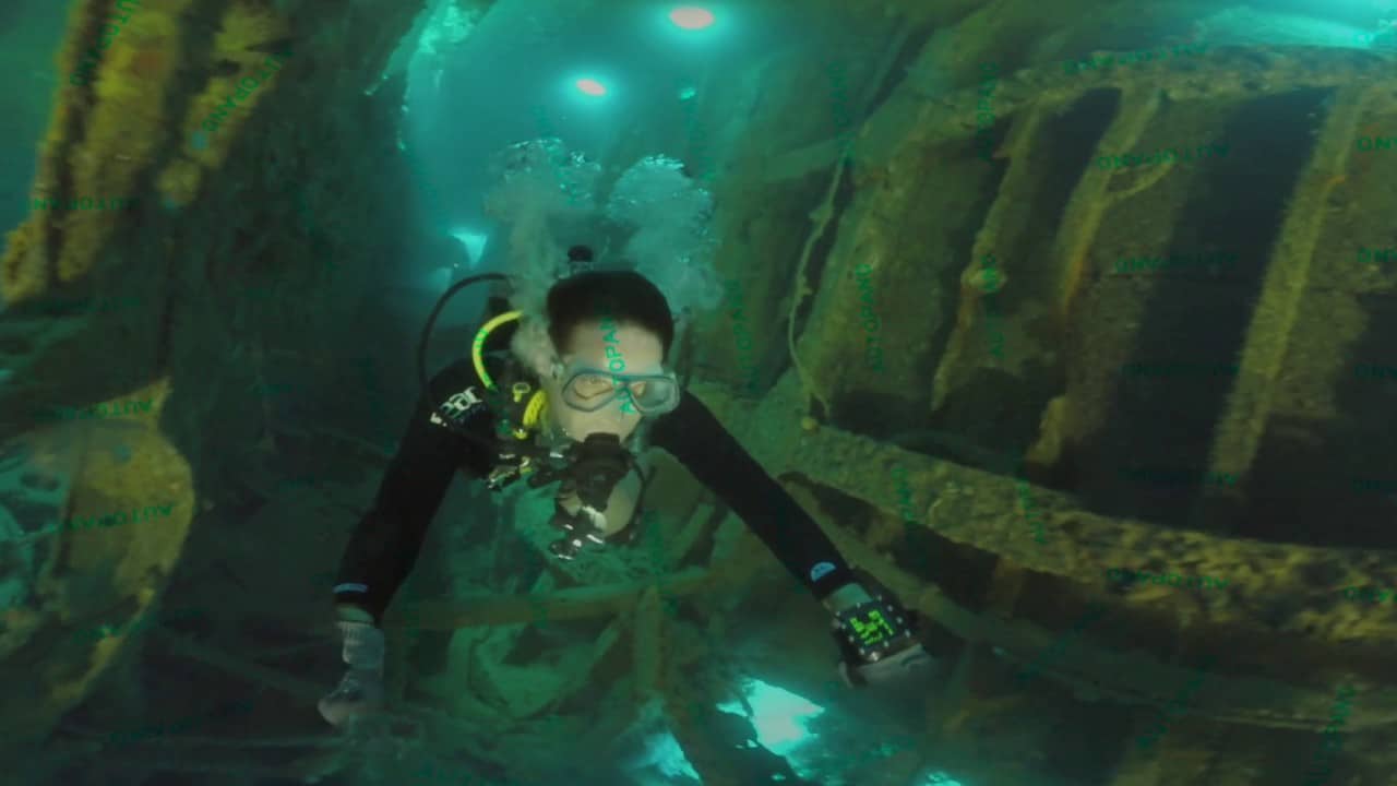 A scuba diver with full gear is exploring a sunken wreck in Coron, swimming through its rusty metal structure as light filters in through the openings above.