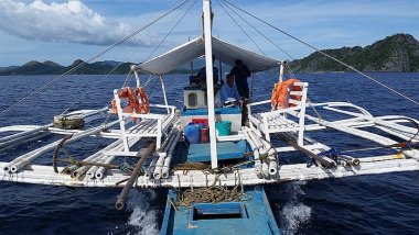 A small white boat with a canopy embarks on an island-hopping tour across the calm blue sea, with lush green islands in the background under a vibrant blue sky.