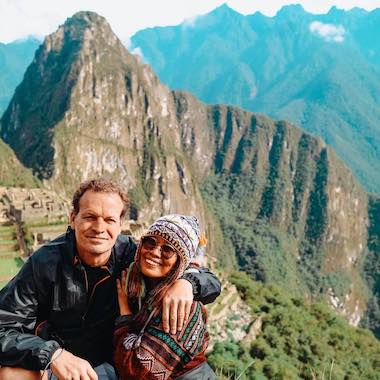 A couple poses with Machu Picchu and lush, green mountains in the background, their smiles bright from a recent island-hopping adventure.