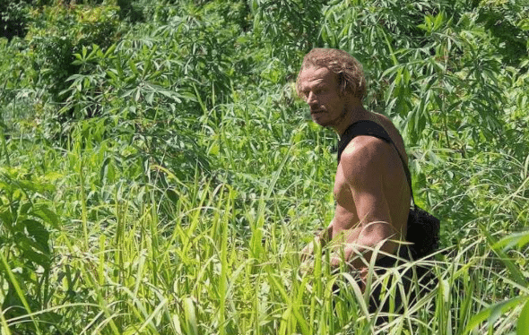 A shirtless man carrying a bag strides through the dense, green vegetation of the jungle on an adventurous excursion near El Nido.