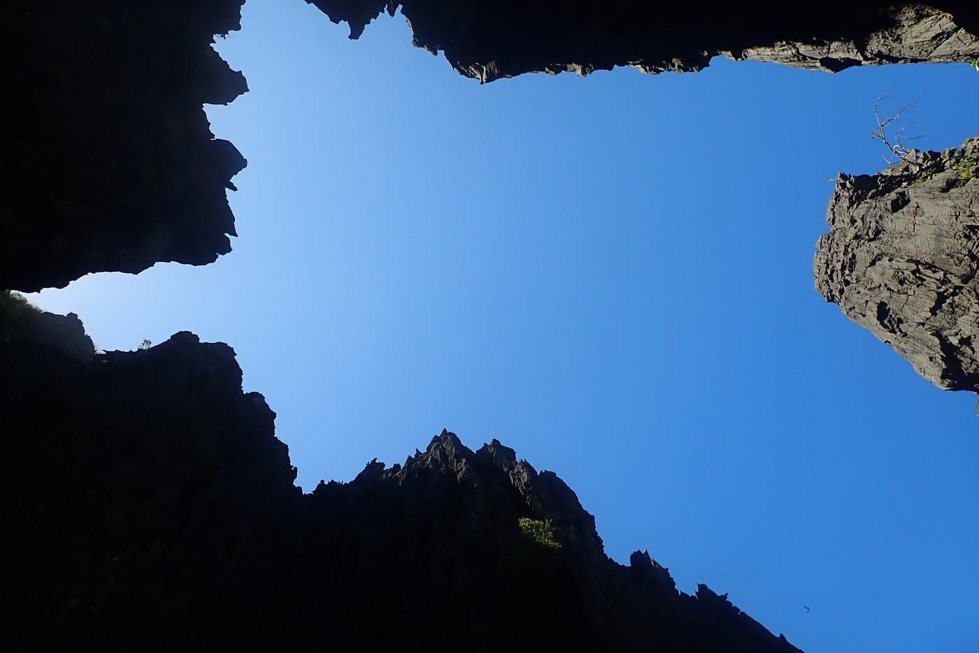 A view from below of a clear blue sky framed by the jagged rock formations of El Nido creates an irregular border around the bright sky, with hints of greenery visible on some of the edges.