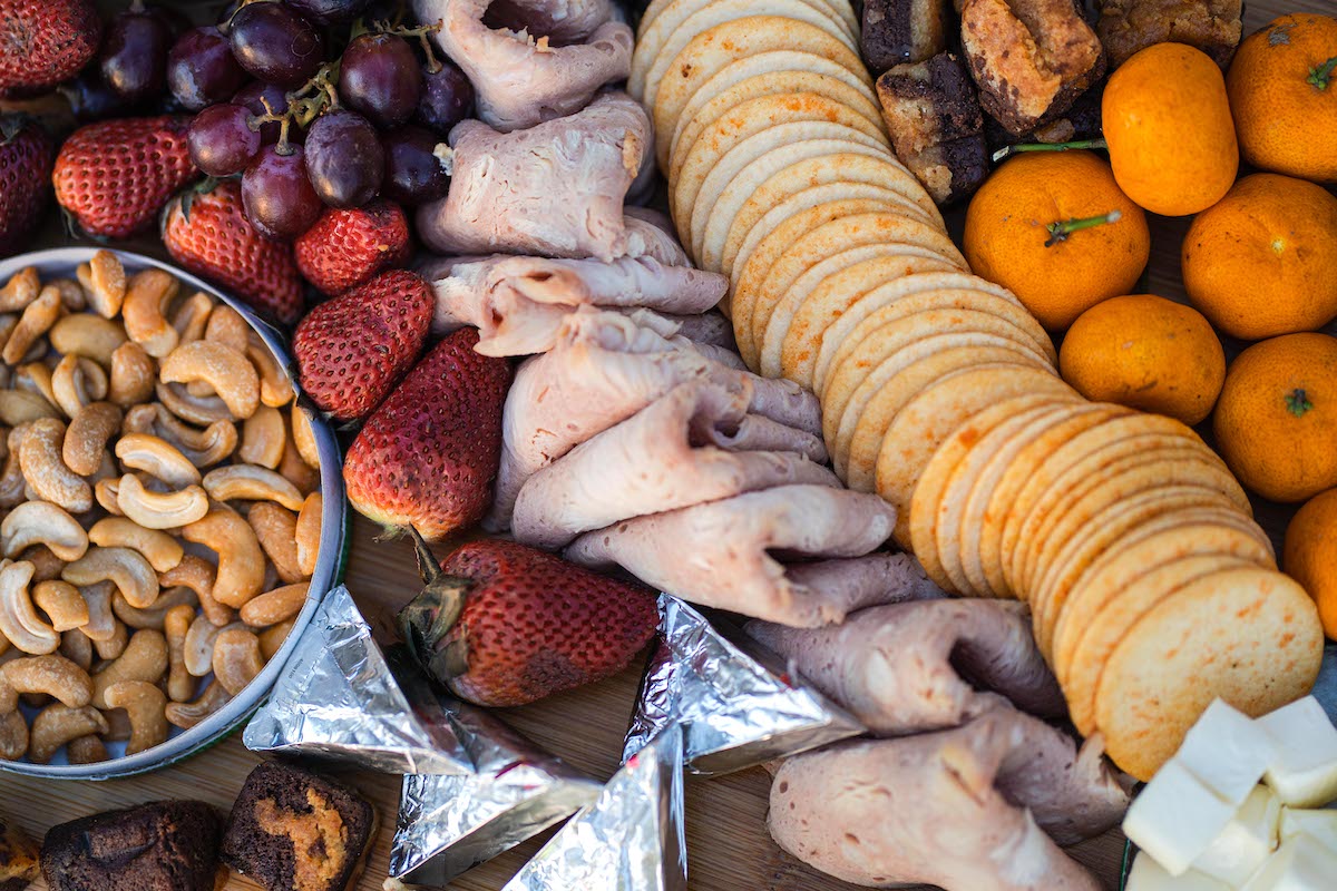 A close-up of a charcuterie board designed for a romantic proposal, featuring sliced turkey, crackers, cashews, strawberries, grapes, tangerines, cheese cubes, chocolate pieces and triangular foil-wrapped cheeses—creating a perfect moment to cherish.