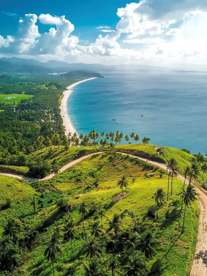 Port Barton beach with lush green hills and palm trees, overlooking the clear blue sea in Palawan.