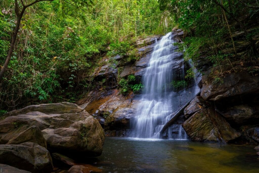 Waterfall in Port Barton surrounded by dense green forest and large rocks.