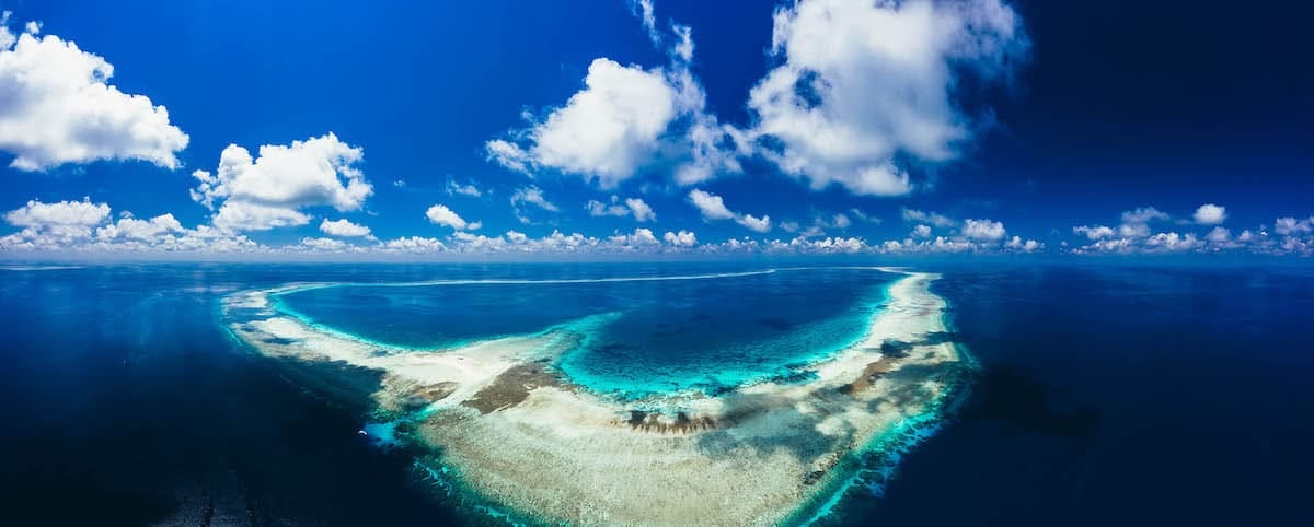 Aerial view of a heart-shaped coral reef near Coron, surrounded by the vibrant turquoise waters and deep blue ocean. Fluffy white clouds dot the clear blue sky, creating a serene and picturesque seascape perfect for unforgettable boat tours. Aerial view of a heart-shaped coral reef near Coron, surrounded by the vibrant turquoise waters and deep blue ocean. Fluffy white clouds dot the clear blue sky, creating a serene and picturesque seascape perfect for unforgettable boat tours.
