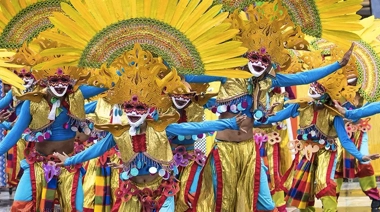 Dancers in vibrant costumes and large, decorative headdresses perform energetically in a colorful festival parade, reminiscent of the lively celebrations you experience during an island-hopping adventure.
