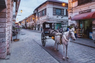 A horse-drawn carriage meanders along a cobblestone street lined with colonial buildings at dusk, capturing the timeless charm akin to an evening boat tour through historic waters.