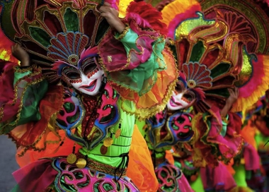 Dancers in vibrant, colorful costumes and masks perform during a festival, showcasing intricate designs and lively expressions, much like the vivid scenes on an island hopping boat tour.