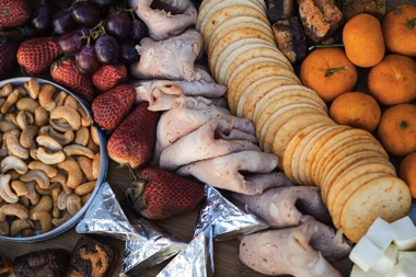 A colorful spread of cashews, strawberries, grapes, turkey slices, crackers, brownies, cheeses, and mandarins is artfully arranged on a wooden board, reminiscent of the diverse flavors experienced on an island hopping boat tour.