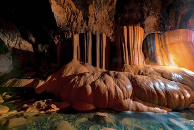 In a dimly lit cave, where stalactites and stalagmites reign, water pools on the ground, crafting a mysterious and serene atmosphere. Nearby, island hopping unveils hidden wonders like this grotto, perfect for those seeking awe beyond the typical boat tour.