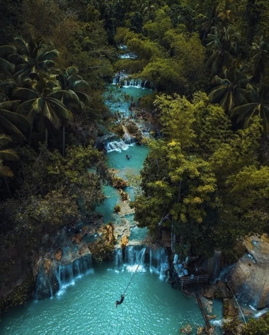 Aerial view of a lush, tropical forest with cascading waterfalls and turquoise pools surrounded by dense green foliage, ideal for an unforgettable island hopping adventure.