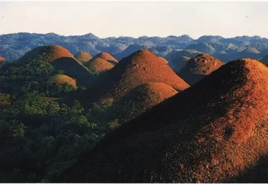 Rolling hills with brown tops set against a backdrop of lush greenery under a clear sky, perfect for an island hopping adventure or a tranquil boat tour.