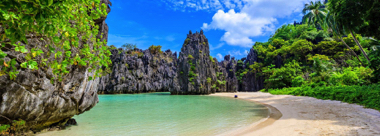 A serene beach with turquoise waters, flanked by towering limestone cliffs and lush greenery under a partly cloudy blue sky, invites you to embark on an island hopping boat tour for an unforgettable adventure.