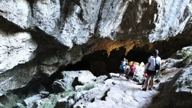 People exploring a rocky cave with uneven terrain under a large stone archway, as part of an adventurous island hopping boat tour.