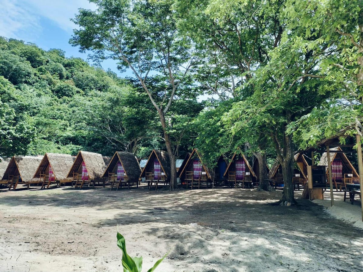 Beautiful traditional Filipino nipa huts set on a sandy beach with lush greenery in the background.