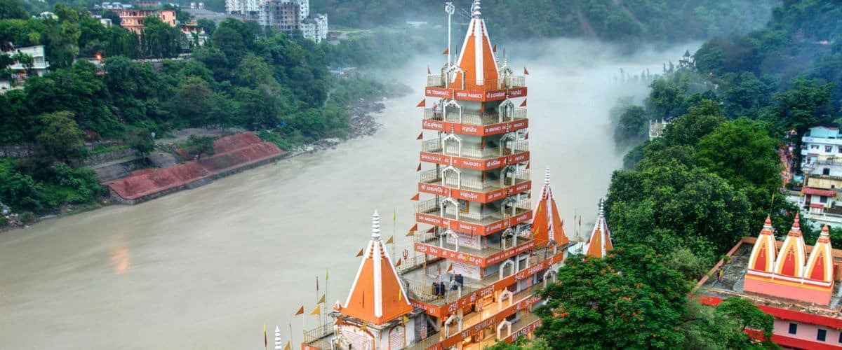 Bright, colorful Hindu temple by a river with lush greenery, vibrant orange rooftops, and intricate architecture.