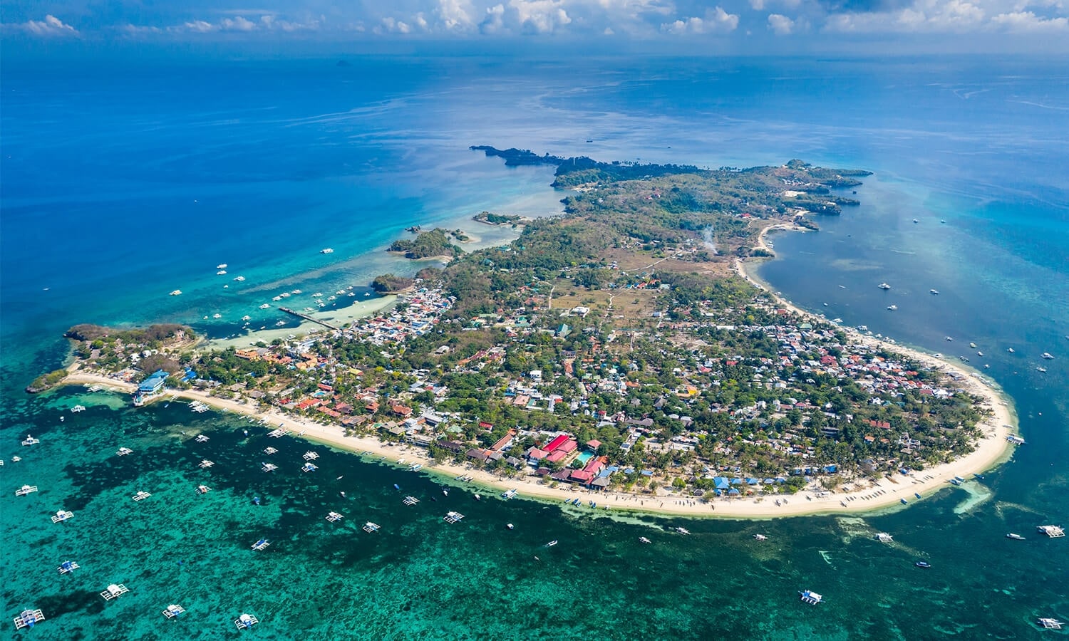 Aerial view of a Philippine island with lush greenery and clear blue sea.
