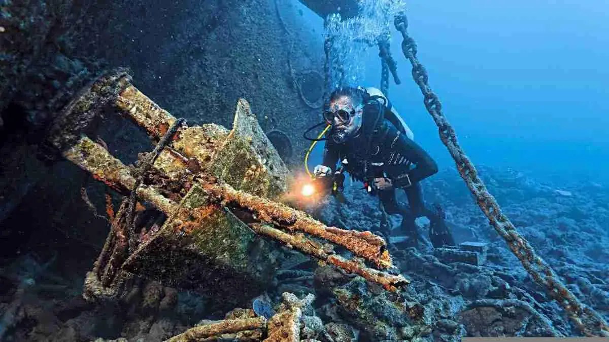 Underwater exploration of a shipwreck with scuba diver illuminating the site.