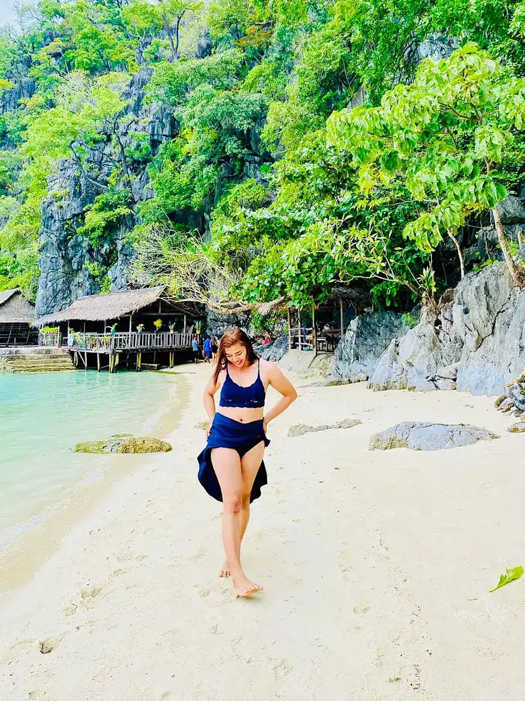 Idyllic island beach with clear waters, lush trees, and a woman enjoying the tropical scenery.