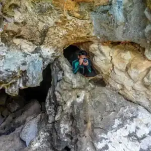 Young woman exploring a cave with a camera among rugged rock formations in the Philippines.