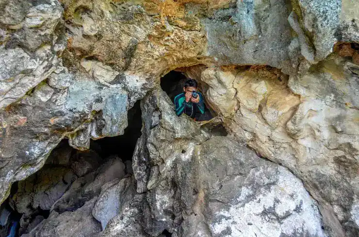 Young woman exploring a cave with a camera among rugged rock formations in the Philippines.