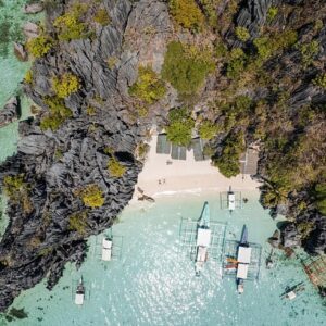 Aerial view of a scenic tropical island featuring crystal-clear waters, boats, and lush rocky cliffs, perfect for travel tips in the Philippines.
