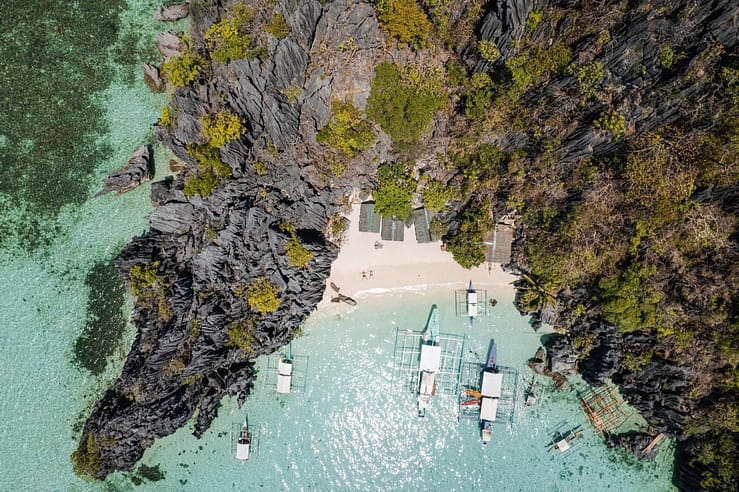 Aerial view of a scenic tropical island featuring crystal-clear waters, boats, and lush rocky cliffs, perfect for travel tips in the Philippines.