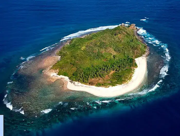 Aerial view of a lush green island with white sandy beaches and vibrant blue ocean waters.