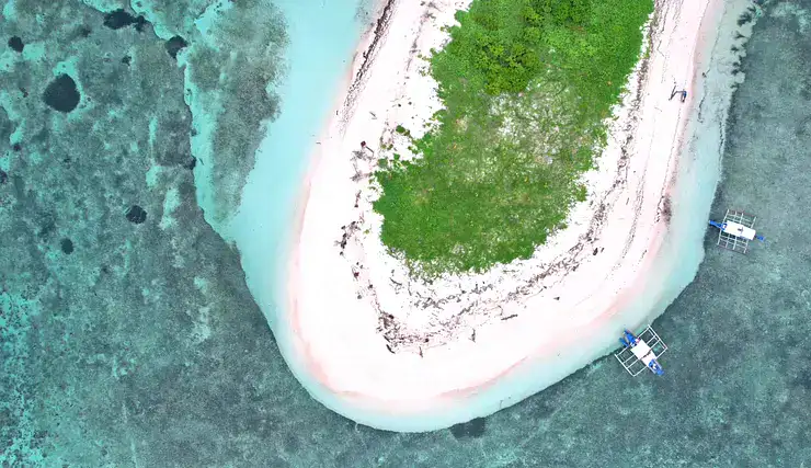 A stunning aerial view of a small tropical island surrounded by turquoise water and boats.