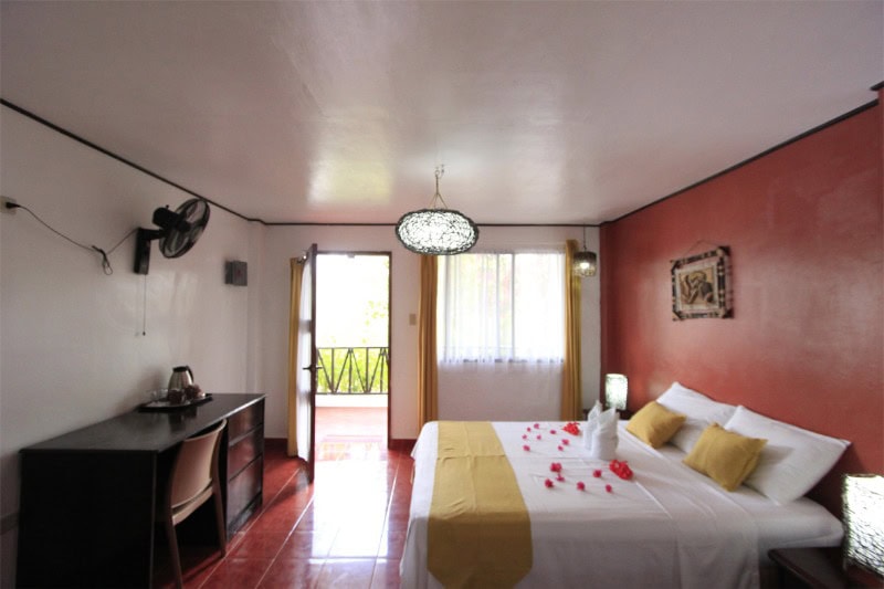 Cozy hotel bedroom with a double bed, yellow accents, and rose petal decor, perfect for a relaxing Philippines getaway.