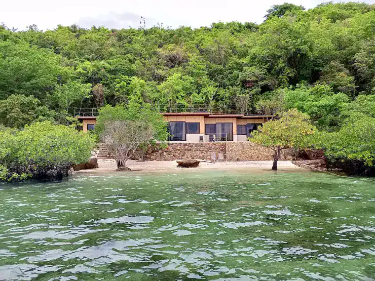 Beachfront villa surrounded by green trees and calm waters, perfect for tropical vacations.