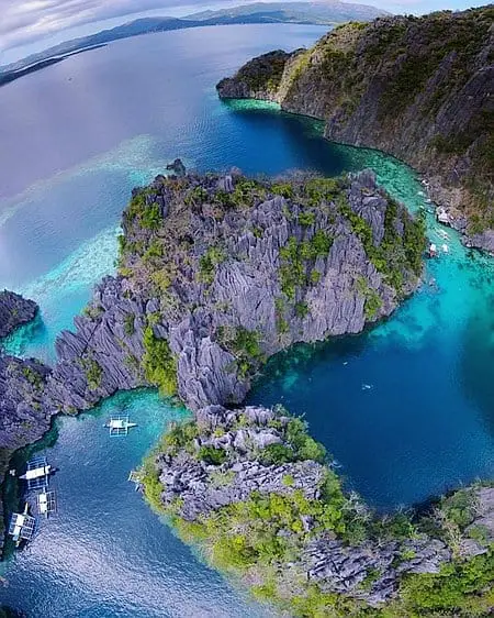 Breathtaking aerial view of a Philippine island surrounded by crystal-clear waters and dramatic rocky cliffs.