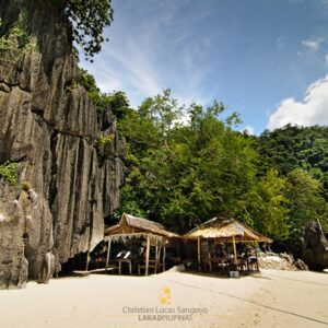 Secluded Filipino beach with rocky cliffs, clear sand, and traditional bamboo huts for travelers.