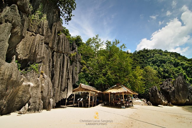 Secluded Filipino beach with rocky cliffs, clear sand, and traditional bamboo huts for travelers.