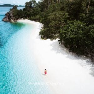 Pristine white beach with clear turquoise waters and lush greenery in the Philippines. Perfect for vacationers.