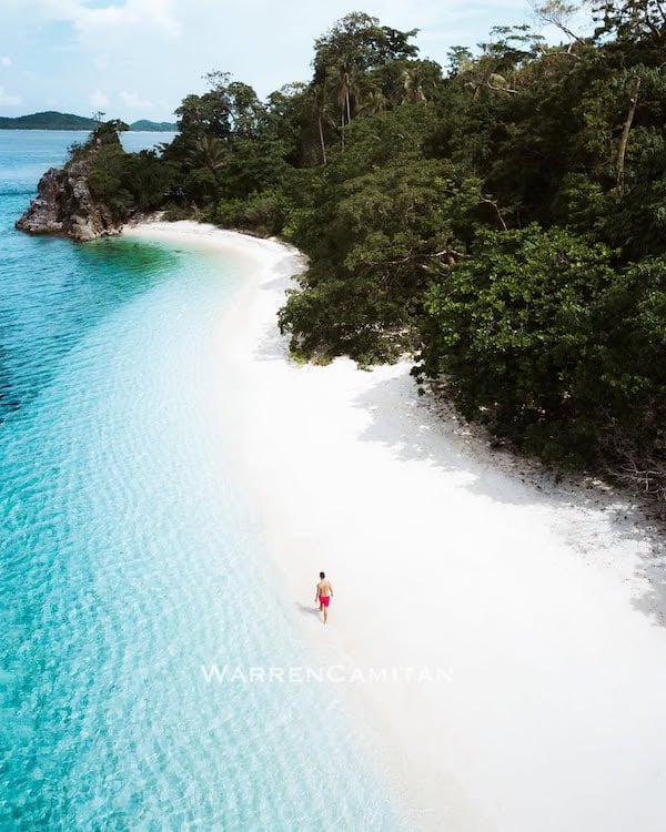 Pristine white beach with clear turquoise waters and lush greenery in the Philippines. Perfect for vacationers.