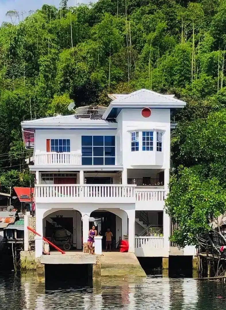 Bright white house built on stilts over the water, surrounded by lush greenery in the Philippines.