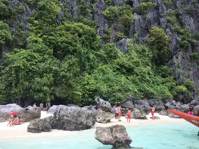 Beautiful beach scene with turquoise water, rocks, and lush greenery in the background.