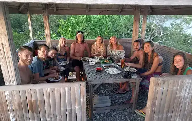 Group of friends enjoying traditional Filipino meal outdoors in a wooden hut.