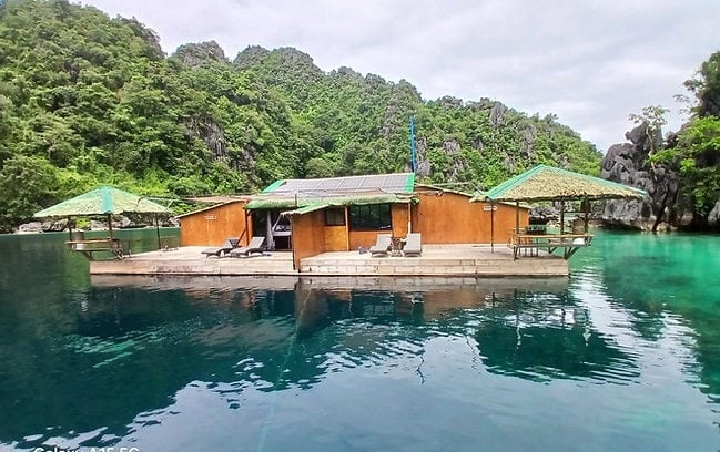 Beautiful floating house in clear blue waters surrounded by lush greenery in Palawan, Philippines.
