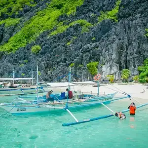 Serene Philippines beach with traditional boats and clear turquoise waters, ideal for island hopping.