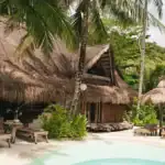 Idyllic tropical island resort featuring traditional thatched-roof huts, outdoor lounge chairs, and lush tropical surroundings.