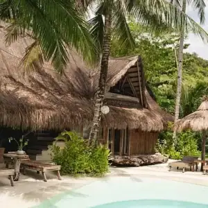 Idyllic tropical island resort featuring traditional thatched-roof huts, outdoor lounge chairs, and lush tropical surroundings.