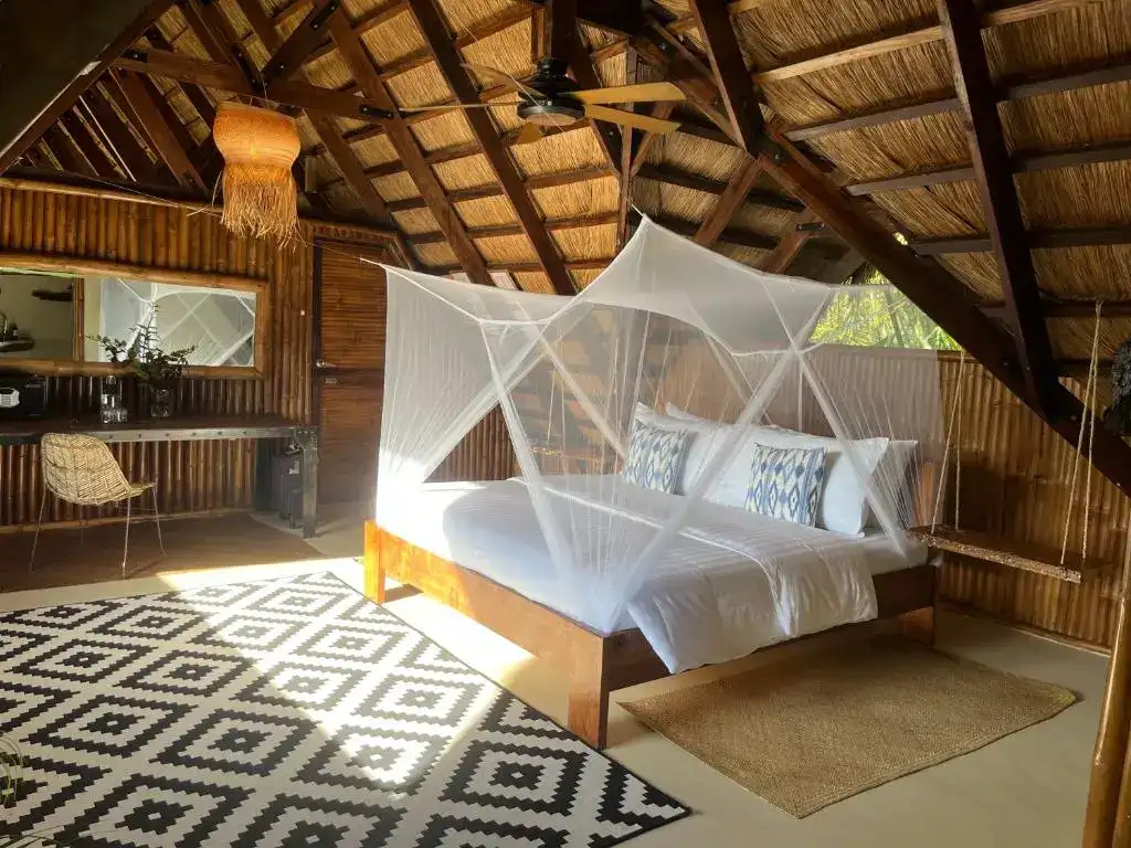 Bright bedroom with mosquito net canopy in a rustic, eco-friendly treehouse in the Philippines.