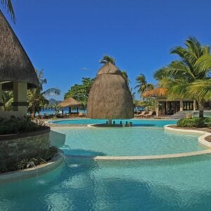 Relaxing poolside at a luxury Filipino island resort surrounded by lush palms and traditional huts.