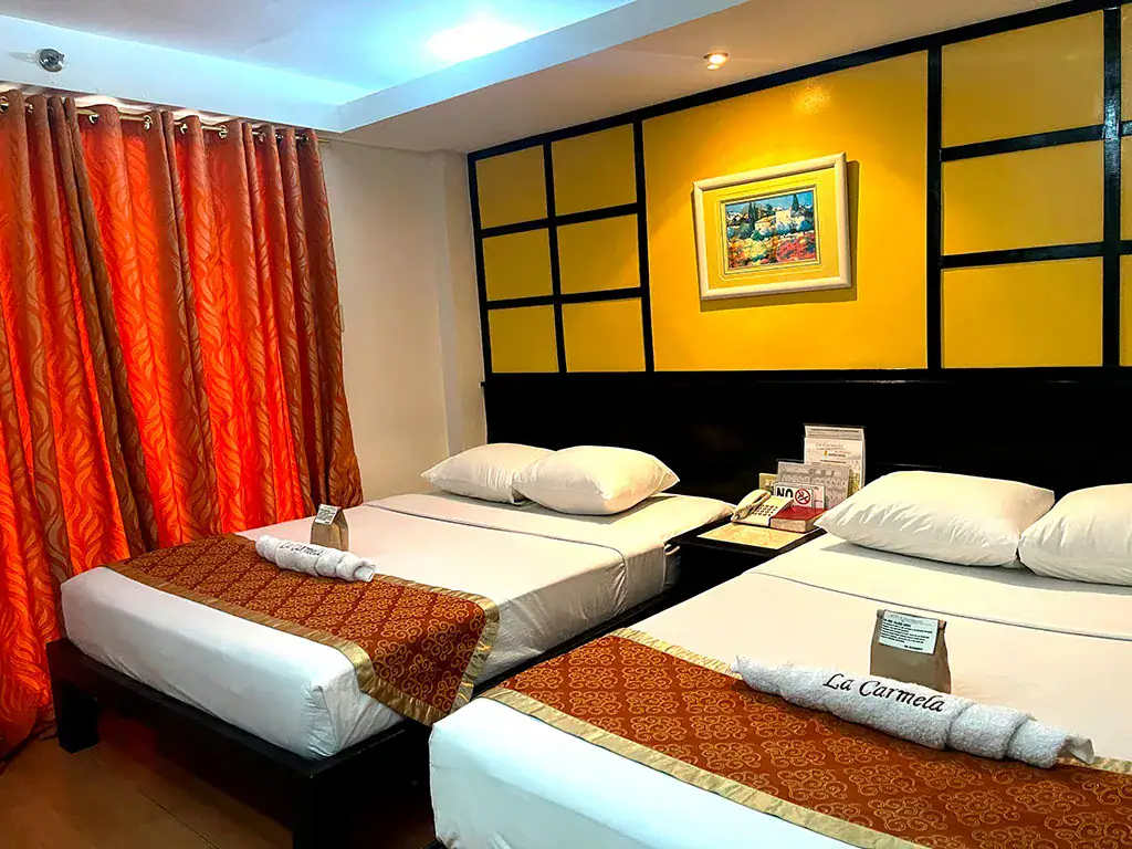 Modern hotel room featuring two beds, warm lighting, and vibrant orange curtains for a relaxing stay.